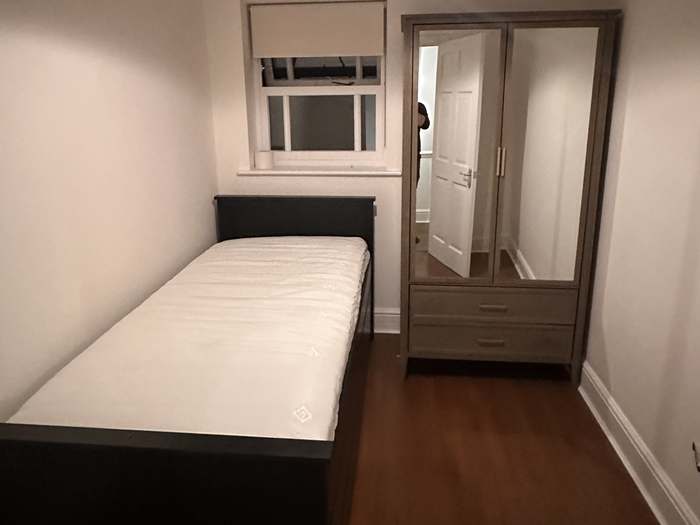A single bed frame and a mirrored wardrobe with drawers, both assembled, in a newly furnished bedroom.