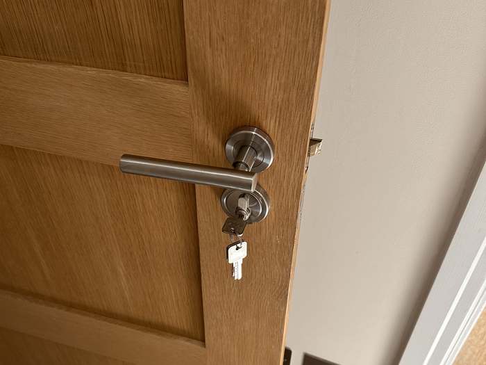 A brushed steel lever handle and keyed lock newly fitted to an oak bedroom door, key in the barrel.